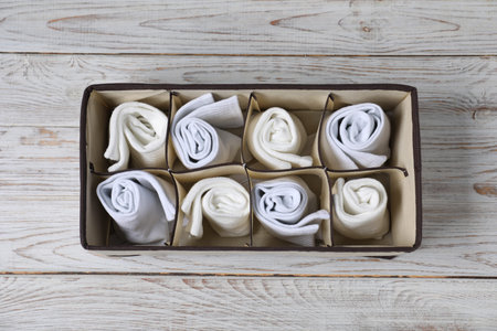 Comfortable white socks in organizer on wooden background, top view