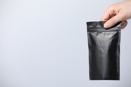 Woman holding blank zipper stand-up pouch on light gray background, closeup. Space for textの写真素材