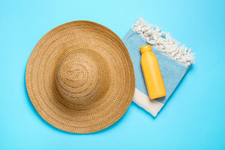 Straw hat, beach towel and sunscreen on light blue background, flat lay