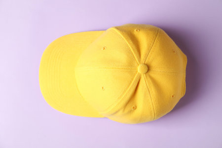 Yellow baseball hat on violet background, top view