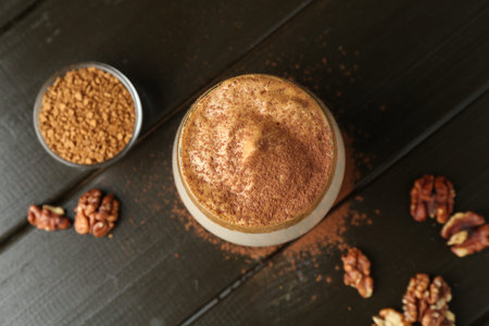 Delicious dalgona coffee in glass, granules, walnuts and brown sugar on wooden table, flat layの写真素材