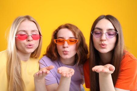 Beautiful women with different hair colors blowing kisses on orange backgroundの写真素材
