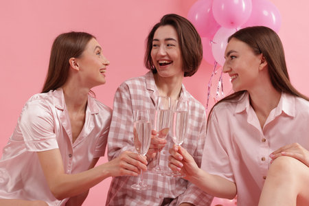 Pajama party. Happy friends clinking glasses on pink backgroundの写真素材