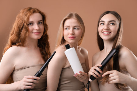 Beautiful women with different hair colors holding curling iron, shampoo and straightener on dark beige backgroundの写真素材