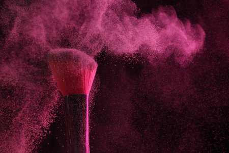 Makeup brush with pink eye shadow on black background, closeup
