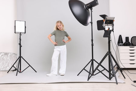 Little girl on light grey background in photo studio with professional equipment