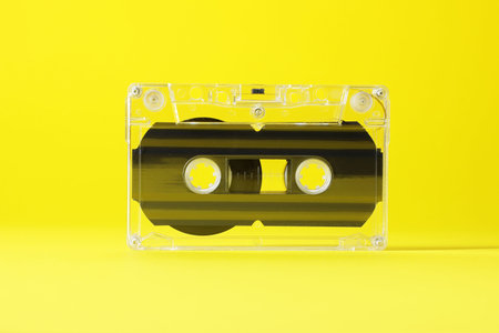 One audio cassette with magnetic tape on yellow background, closeup