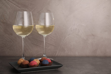 Tasty wine in glasses and truffle bonbons on grey table, space for text