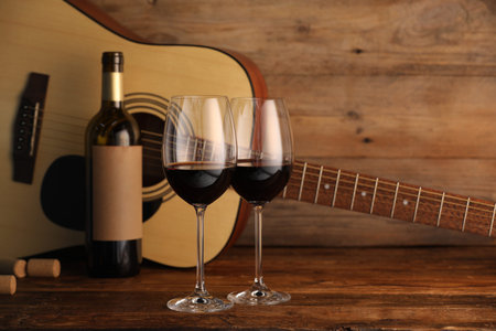 Acoustic guitar, bottle and glasses of red wine on wooden table. Space for textの写真素材