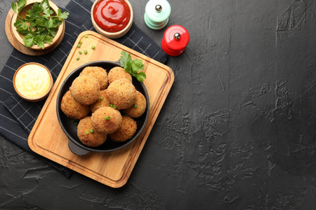 Delicious fried croquette balls with green onion, parsley, sauces and spices on dark textured table,...