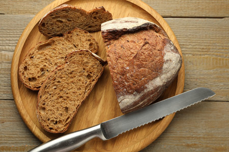 Pieces of fresh bread and knife on wooden table, top view