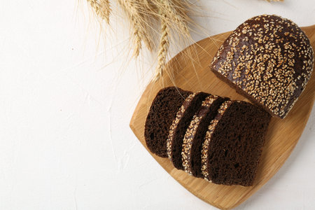 Pieces of fresh rye bread with seeds and spikes on white table, flat lay. Space for text