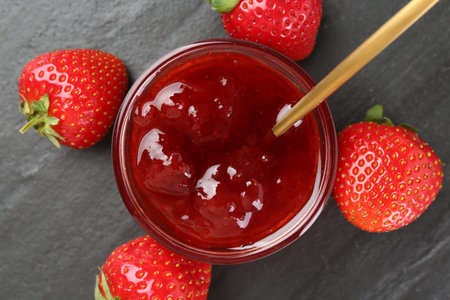 Tasty homemade strawberry jam and berries on black table, top view