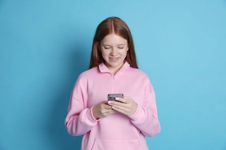 Smiling teenage girl using smartphone on light blue backgroundの写真素材