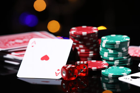 Casino chips, playing cards and dice on mirror surface against blurred lights, closeup