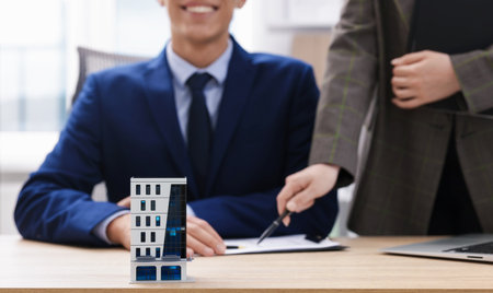 Real estate agent working with client at desk in office, focus on house modelの写真素材