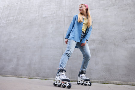 Beautiful young woman with roller skates near gray wall outdoors, low angle view