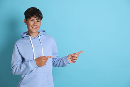 Teenage boy pointing at something on light blue background, space for text