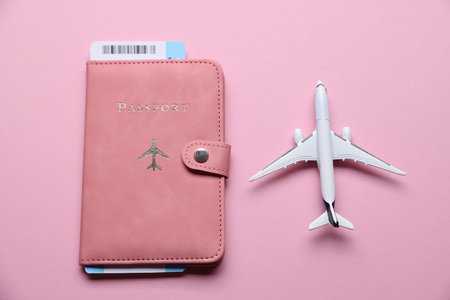 Airplane model, flight ticket and passport on pink background, flat lay