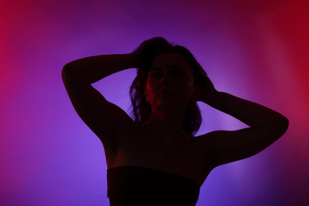 Silhouette of woman posing in neon lights on color background