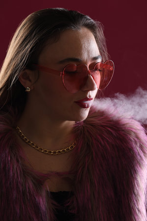 Beautiful woman in fur coat smoking on dark pink background, closeup