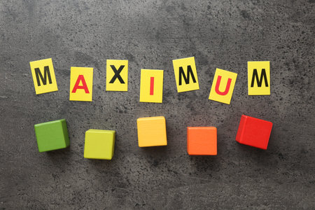 Word Maximum and colorful cubes on grey table, flat lay