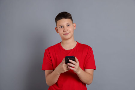 Teenage boy with smartphone on grey background