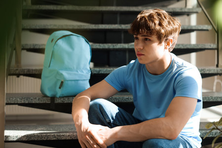 Teen problems. Upset teenage boy on stairs indoors