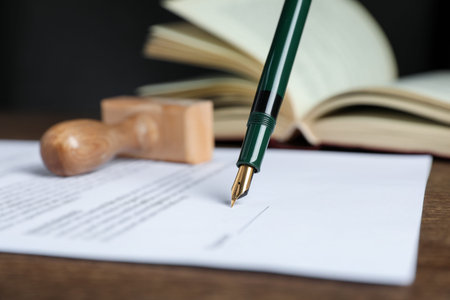 Signing notary document with fountain pen at wooden table against black background, closeup