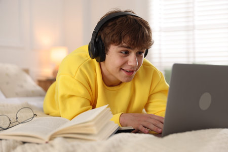 Teenage student using laptop while studying on bed at homeの写真素材