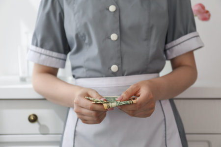 Chambermaid counting tips leaning chest of drawers in hotel room, closeup. Gratuity for workの写真素材