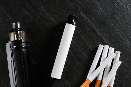 Electronic smoking devices and cigarettes on black table, flat lay