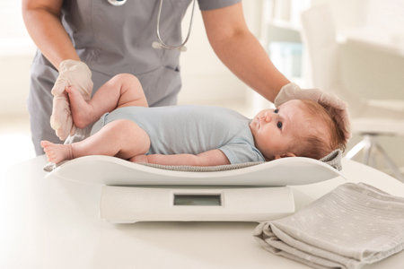 Pediatrician weighting baby with scales at white table in clinic, closeupの写真素材