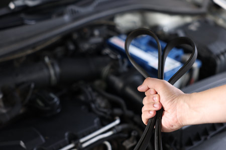 Auto mechanic with timing belt near open hood of car indoors, closeup. Space for text