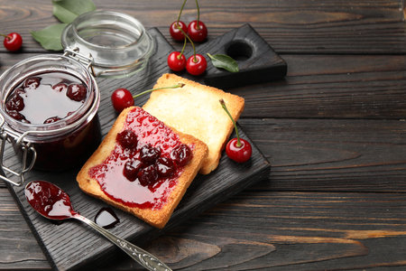 Toasts with tasty cherry jam and fresh fruits on black wooden table, closeup. Space for text