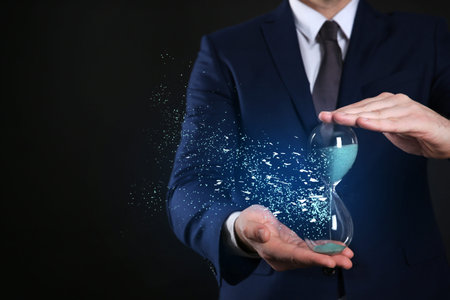 Time running out. Hourglass dissolving in man's hands against black background, closeup