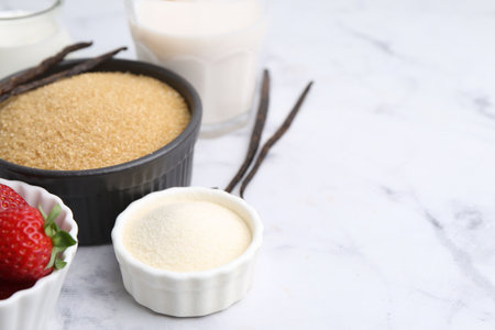 Different ingredients for panna cotta. Milk, sugar, vanilla and strawberries on white marble table, closeup. Space for textの写真素材