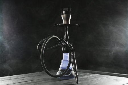 Hookah on wooden table with smoke against black background
