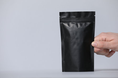 Woman holding blank zipper stand-up pouch on light grey background, closeup. Space for text