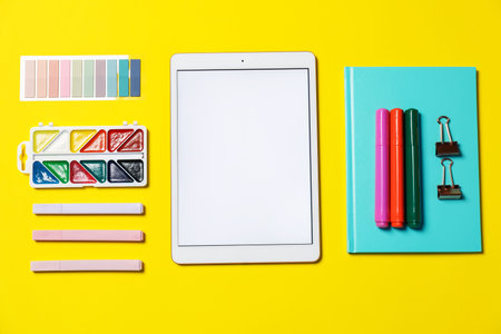 Tablet and different stationery on yellow background, flat lay