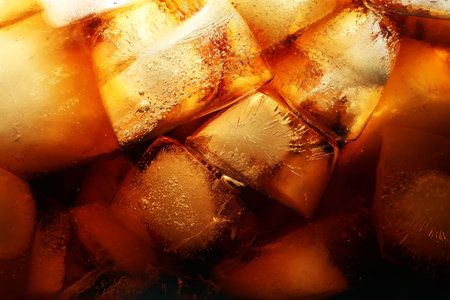Refreshing cola with ice as background, macro view