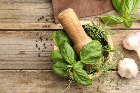Mortar with pestle, different aromatic herbs and spices on wooden table, flat lay. Space for text
