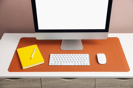 Stylish workplace with computer and orange mousepad on white table indoors, closeup