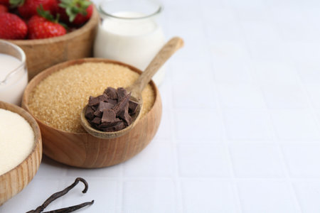 Different ingredients for panna cotta. Milk, sugar, vanilla, chocolate and strawberries on white tiled table, closeup. Space for textの写真素材