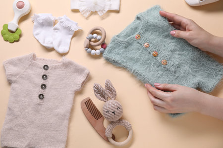 Woman with baby clothes and accessories on beige background, top view