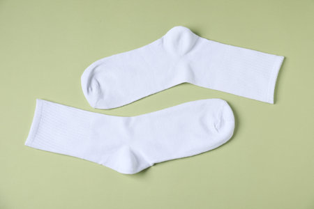 Pair of comfortable white socks on light green background, top view
