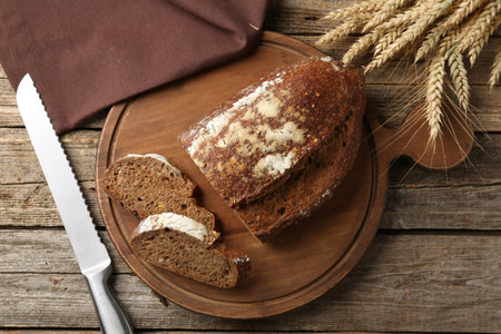 Pieces of fresh rye bread, knife and spikes on wooden table, flat lay