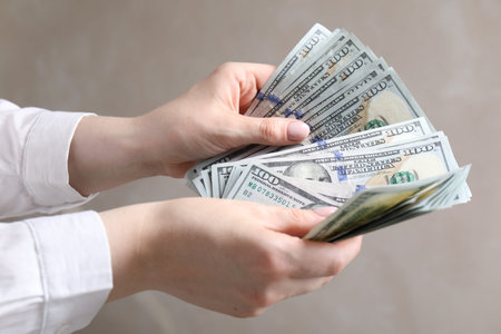 Woman counting dollar banknotes on beige background, closeup