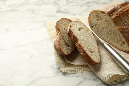 Pieces of fresh bread and knife on white marble table, closeup. Space for text