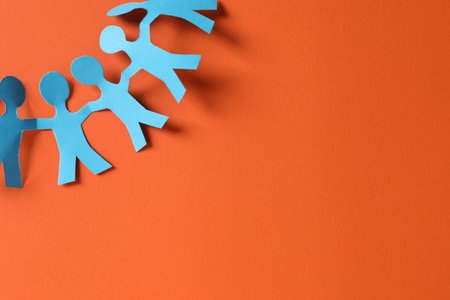 Paper figures of people holding hands on orange background, top view. Space for text